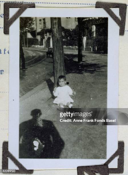 Margot Frank, older sister to Anne Frank, sitting against a pole with a person's shadow in the foreground, taken from Margot's photo album.