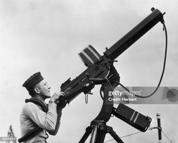 Side view of a soldier aiming a fifty caliber anti-aircraft machine gun in the air, 1940s. He wears a cap and eyeglasses.
