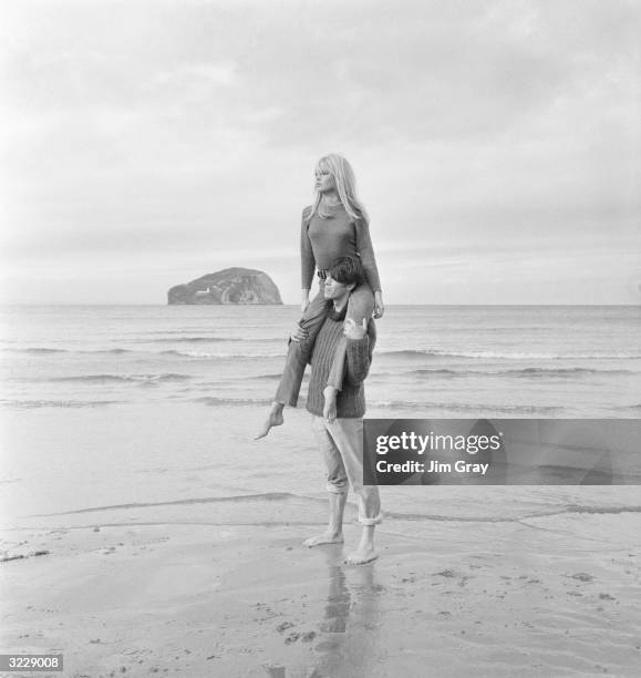 French actor Laurent Terzieff giving Brigitte Bardot a piggy-back ride on the windy beach at North Berwick, Scotland, in a scene from the film 'Two...