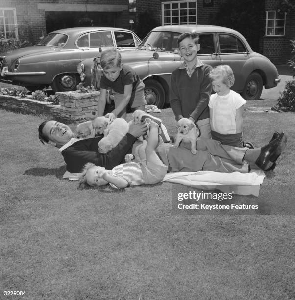 English cricketer Colin Cowdrey is overrun by puppies in the garden of his family home in Surrey.