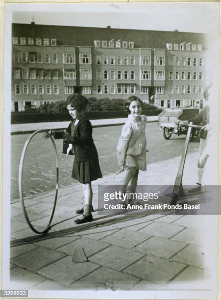 Anne Frank plays with a jump rope as her friend Sanne Ledermann plays with a hoop on a sidewalk in Amsterdam, Holland. Taken from the photo album of...