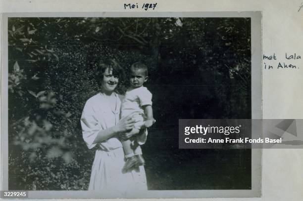 Lala holds frowning baby Margot Frank, the sister of Anne Frank, in her grandmother's garden, Aachen, Germany. Taken from the photo album of Anne...