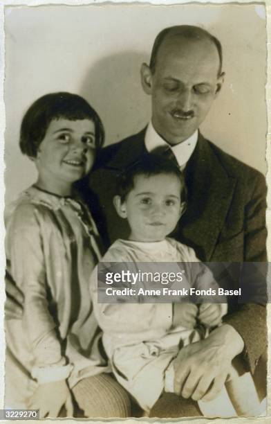Portrait of Otto Frank holding his daughters, Margot and Anne on his lap, taken from the photo album of Anne Frank, Frankfurt am Main, Germany.
