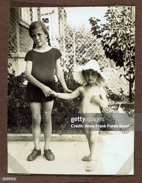 Full-length portrait of Margot Frank , the older sister of Anne Frank, in a hat and underwear, holding hands with her friend Gertrud Naumann,...