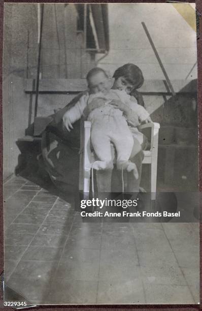 Margot Frank holding her sister Anne Frank on her lap while sitting in a chair on a balcony, Frankfurt am Main, Germany. From Margot Frank's photo...