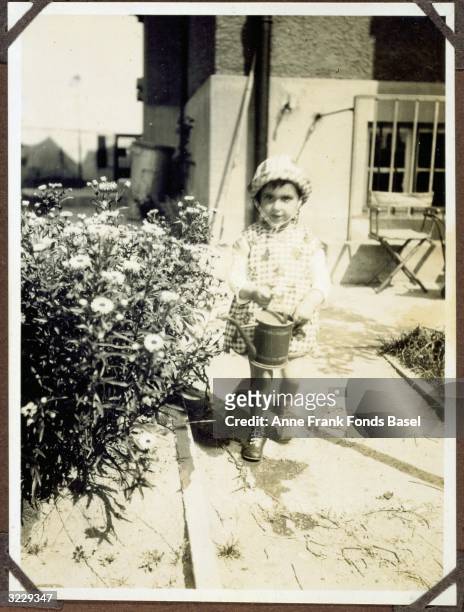 Full-length portrait of Margot Frank, the older sister of Anne Frank, holding a watering pitcher next to flowers in a garden, Frankfurt am Main,...