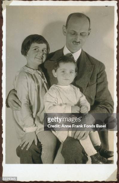 Family portrait of Otto Frank and his daughters Margot and Anne Frank sitting on his lap, Frankfurt am Main, Germany. From Margot Frank's photo album.