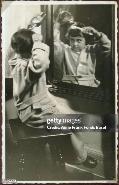 Margot Frank, the older sister of Anne Frank, pouring liquid on her hair while combing it in front of a mirror, Frankfurt am Main, Germany. From...