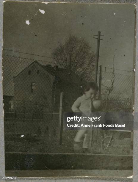 Anne Frank playing with a ball on a street curb in front of a fence, Frankfurt am Main, Germany. Behind her is a tricycle. From Anne Frank's photo...