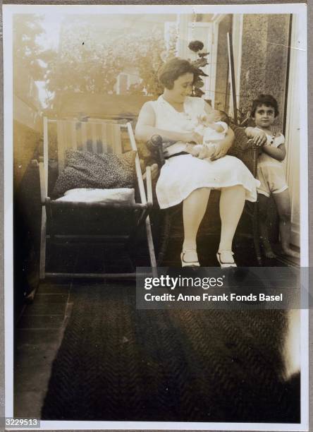 Edith Frank-Hollander holding infant daughter Anne Frank on her lap with daughter Margot Frank standing next to them on a balcony, Marbachweg,...