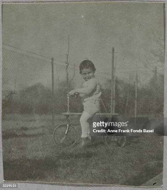 Full-length portrait of Anne Frank sitting on a tricycle, Frankfurt am Main, Germany. From Anne Frank's photo album.