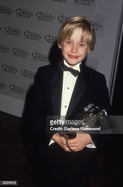 American child actor Macaulay Culkin smiles while holding an award in a tuxedo backstage at the American Comedy Awards. Culkin won Funniest Actor in...