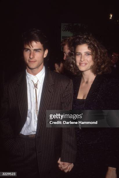 American actor Tom Cruise and his future wife, actor Mimi Rogers, hold hands while standing indoors at the Los Angeles premiere of director Martin...