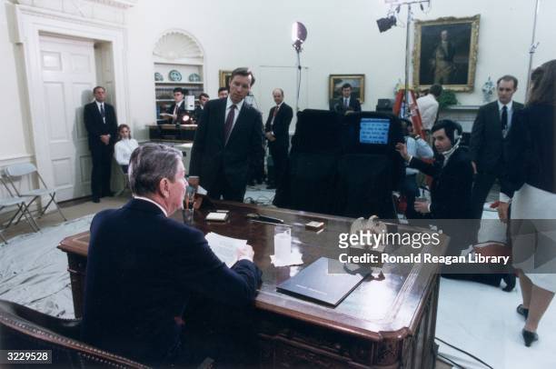 Rear view of US President Ronald Reagan at his desk in the Oval Office, looking at a teleprompter as he delivers his televised farewell address to...