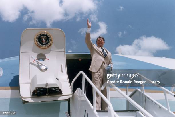 President Ronald Reagan waves as he stands at the top of a stairway, preparing to board Air Force One, Dothan, Alabama, . The door of the aircraft is...