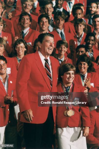 President Ronald Reagan stands with his arm around the shoulders of US Olympic champion gymnast Mary Lou Retton, as other Olympic athletes clap...