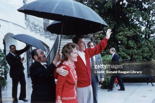 President Ronald Reagan smiles and waves as he stands under an umbrella with First Lady Nancy Reagan after leaving George Washington Hospital,...