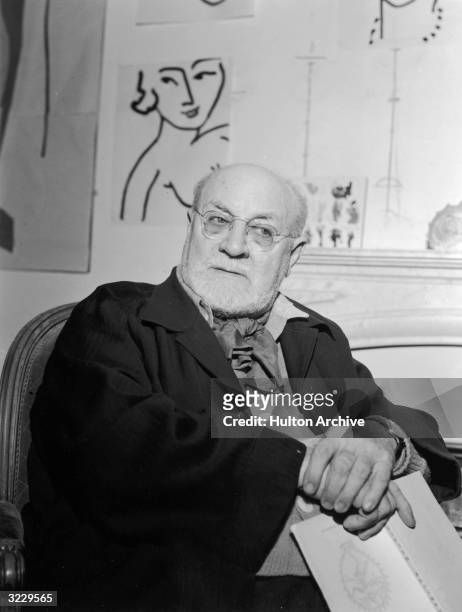 French artist Henri Matisse holds a book while sitting at his villa, 'Le Reve,' in Vence, near Nice, South of France. A line drawing of a woman hangs...