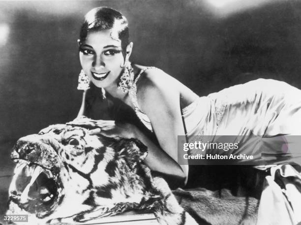 Portrait of American-born singer and dancer Josephine Baker lying on a tiger rug in a silk evening gown and diamond earrings.