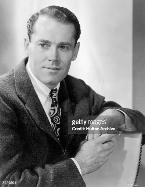Studio portrait of American actor Henry Fonda smiling while leaning against the back of his chair.