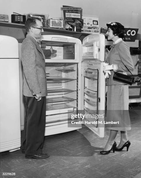 An appliance salesman smiles as he shows the inside of a new refrigerator to a housewife in a store.