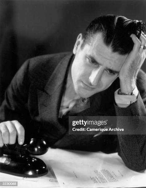 Man leans his head on his hand and knits his brow with concern while holding a telephone receiver. He props his elbow on top of a business letter.