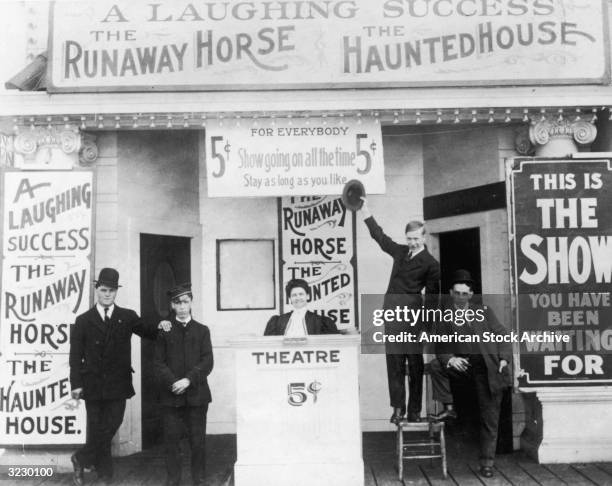 Barkers and ticket takers pose outside the entrance of a nickelodeon theater. Signs advertise three shows: 'A Laughing Success,' 'The Runaway Horse,'...