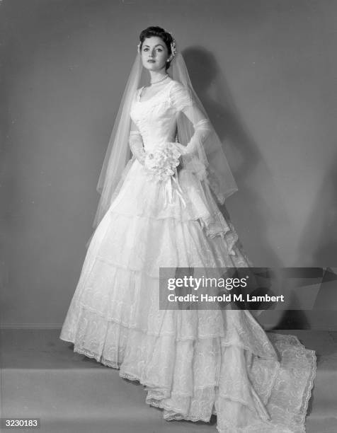 Full-length studio portrait of a bride wearing her wedding gown and veil and holding a bouquet