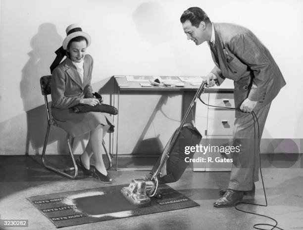 Salesman demonstrates the effectiveness of a General Electric vacuum cleaner to a prospective customer.