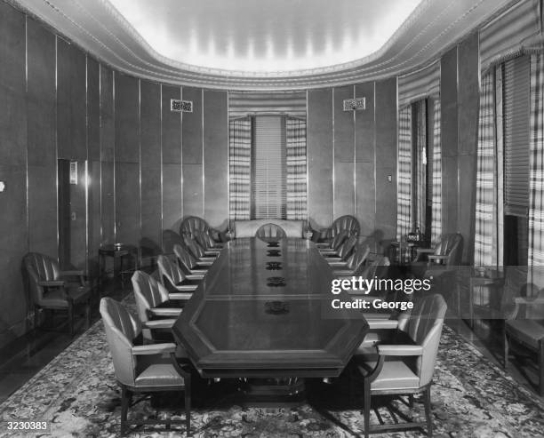 Interior view of an empty boardroom, which has chairs with leather upholstery at a long wooden conference table. There is an oriental rug on the...