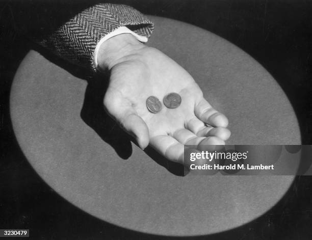 Closeup of a man holding two pennies in his palm, illuminated by a spotlight.