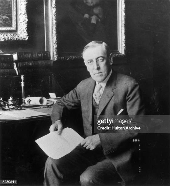 Portrait of U.S. President Woodrow Wilson sitting at a desk, holding a letter.