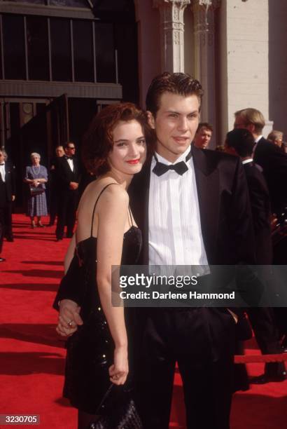 American actors Christian Slater and Winona Ryder pose while holding hands on the red carpet, as they attend the Academy Awards at the Shrine...