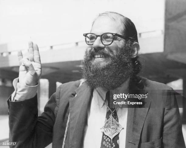 American 'beat' poet Allen Ginsberg smiles while gesturing at a reading of his poetry at Queen Elizabeth Hall, London, England. He wears a 'God's...