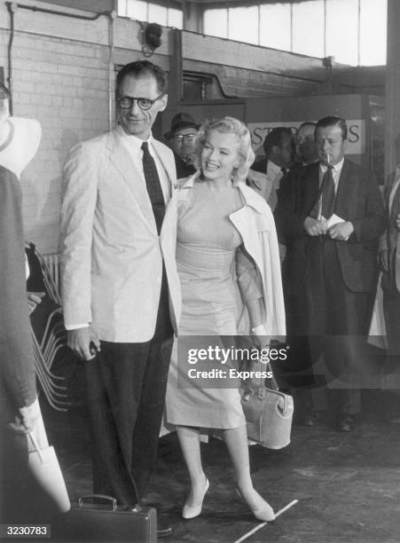 Full-length image of American actor Marilyn Monroe laughing while standing with her husband, American playwright Arthur Miller, after arriving at...