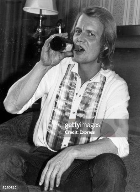 American actor and pop singer David Soul takes a drink from a bottle of lager beer while sitting on a sofa, shortly before the start of his 13-city...