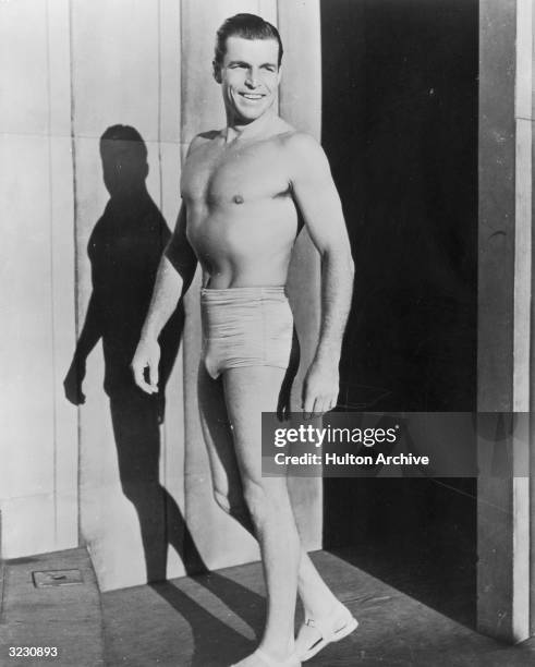 American Olympic swimming champion, turned film actor, Buster Crabbe , wearing swimming trunks and sandals.