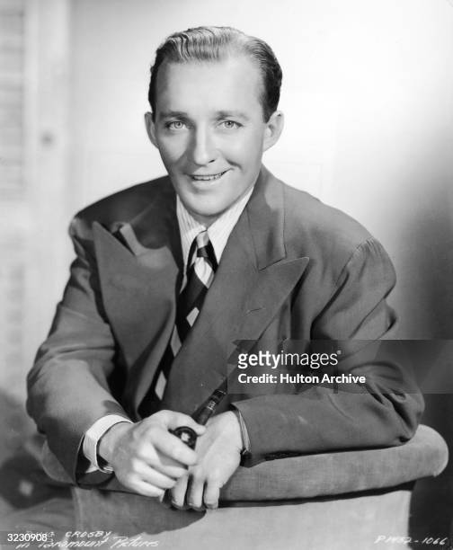 Portrait of American singer and actor Bing Crosby wearing a wide-lapelled suit and holding a pipe.