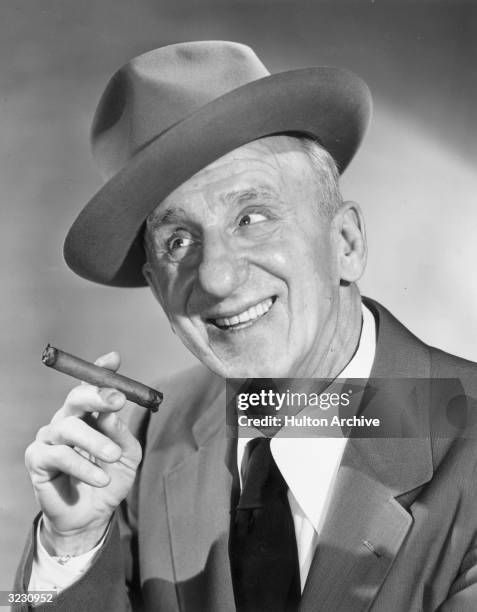 American comedian Jimmy Durante smiling and holding a cigar. He wears a hat at an angle.