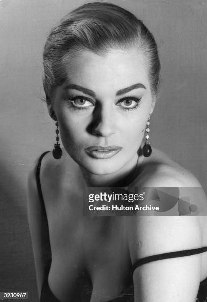 Swedish actress Anita Ekberg, with one strap of her gown hanging over her shoulder. She wears her hair back, with earrings.