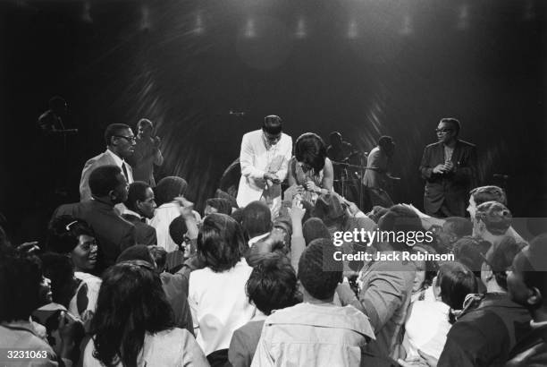 American R&B singer Aretha Franklin bending down onstage to shake hands with a crowd of fans, at the 'Soul Together' concert at Madison Square...