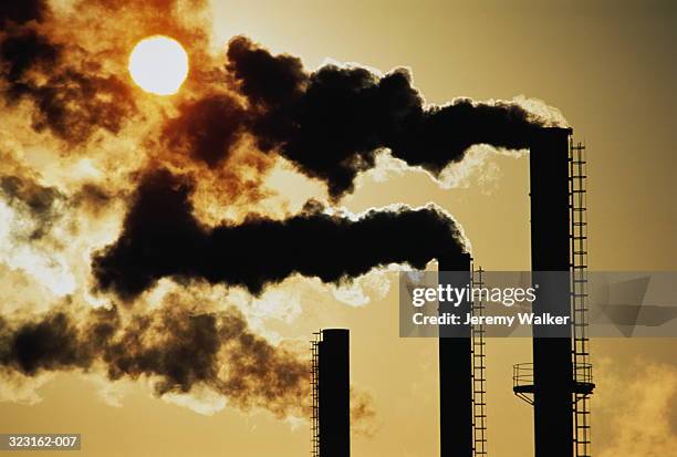 trio of industrial chimneys emitting smoke,sunset,silhouette - inquinamento dellaria foto e immagini stock