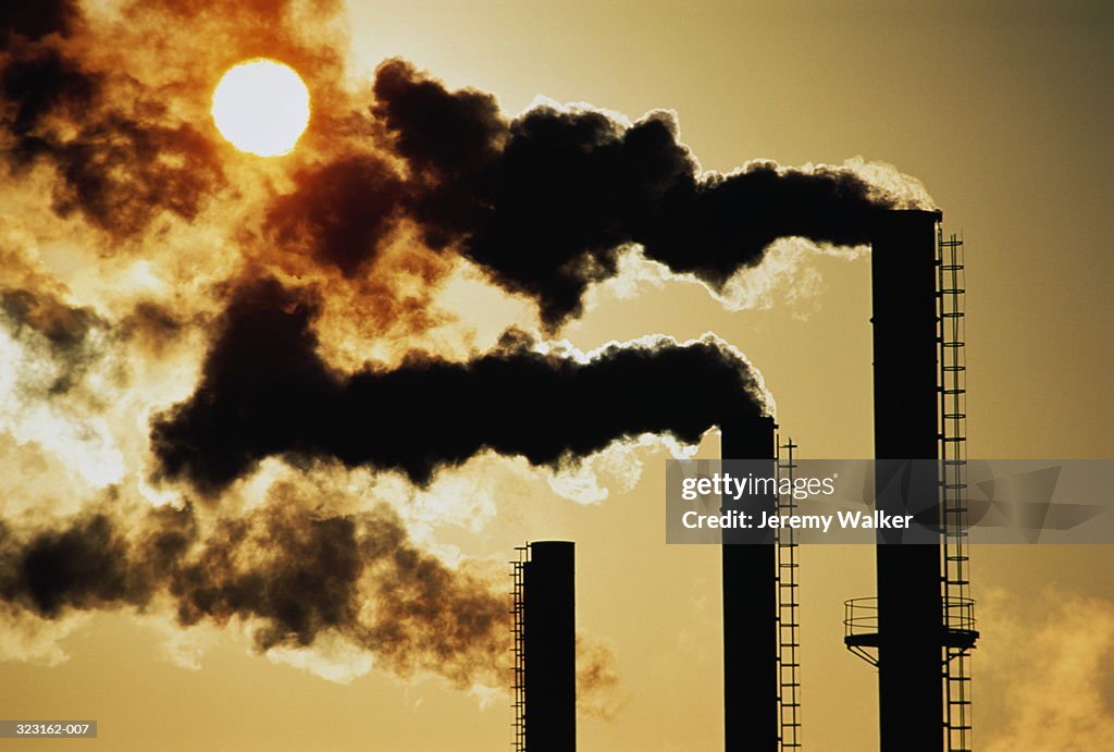 Trio of industrial chimneys emitting smoke,sunset,silhouette