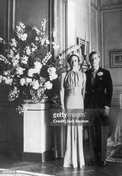 Full-length portrait of the Duke of Windsor and Wallis Warfield posing next to a floral arrangement after their wedding in the Chateau de Conde, near...