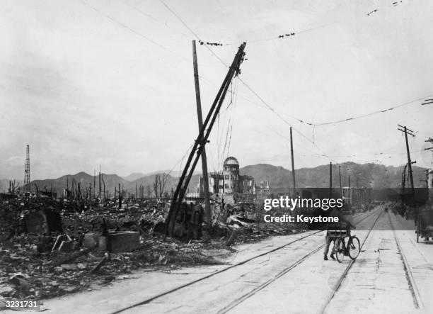 Man wheels his bicycle thorough Hiroshima, days after the city was leveled by an atomic bomb blast, Japan. The view here is looking west-northwest,...