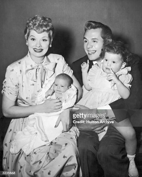American actors and comedian Lucille Ball and her husband, Cuban-born actor and bandleader Desi Arnaz , laugh and smile while holding their two...