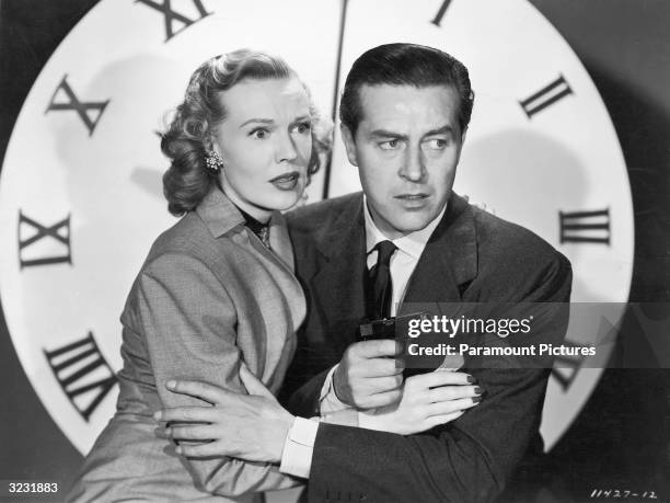 American actor Rita Johnson and Welsh-born actor Ray Milland , holding a gun, embrace in front of a large clock face in a still from director John...