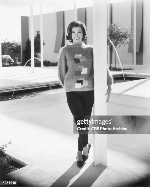 Full-length portrait of American actress Mary Tyler Moore standing outdoors on a patio near two fountains, wearing a sweater and capri pants.