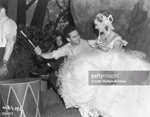 French-born director William Wyler and American actor Bette Davis hold long cigarette filters while laughing on the set of Wyler's film, 'Jezebel,'....