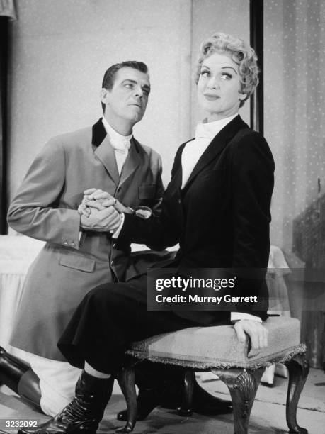 American actor Eve Arden sits on a footstool as her husband, Brooks West, kneels next to her, holding her hand, in the West Coast stage production of...